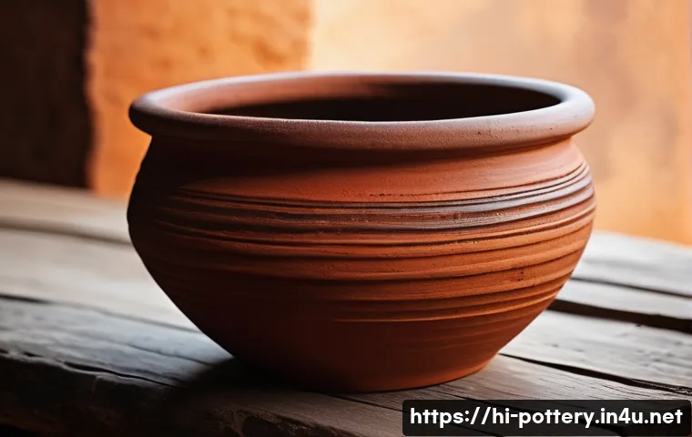 수제 도자기와 기계 생산 비교 - A close-up of a handcrafted clay pot with visible irregularities and unique textures, showcasing the...